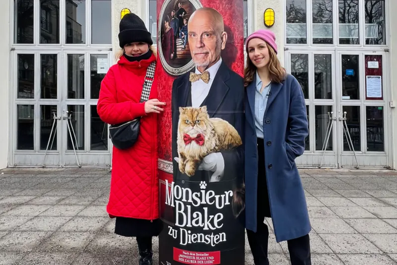 Backstage Digital entdecken: Zwei Frauen vor einem Kino neben einer Plakatsäule für Monsieur Blake zu Diensten